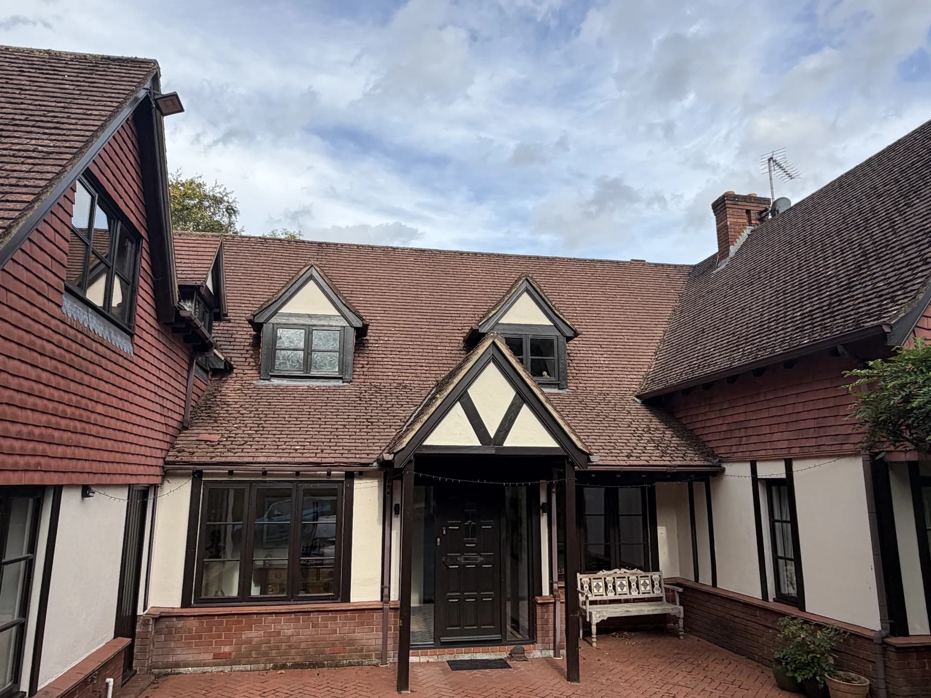 Wide front elevation of the house, courtyard entrance and bench.