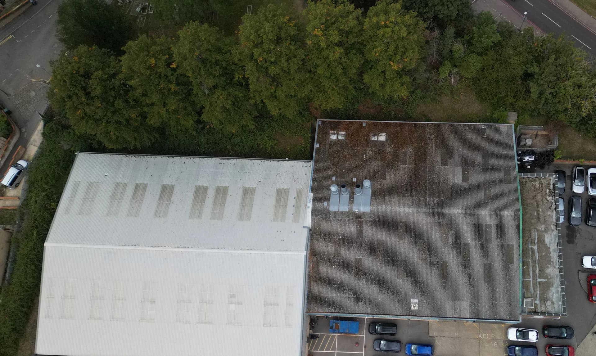 Wide oblique aerial view of an industrial unit with its roof, an adjoining unit and a car yard
