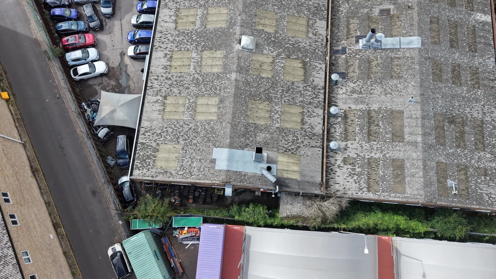 Wide top-down aerial view of mossed roof sheeting beside a yard with parked vehicles