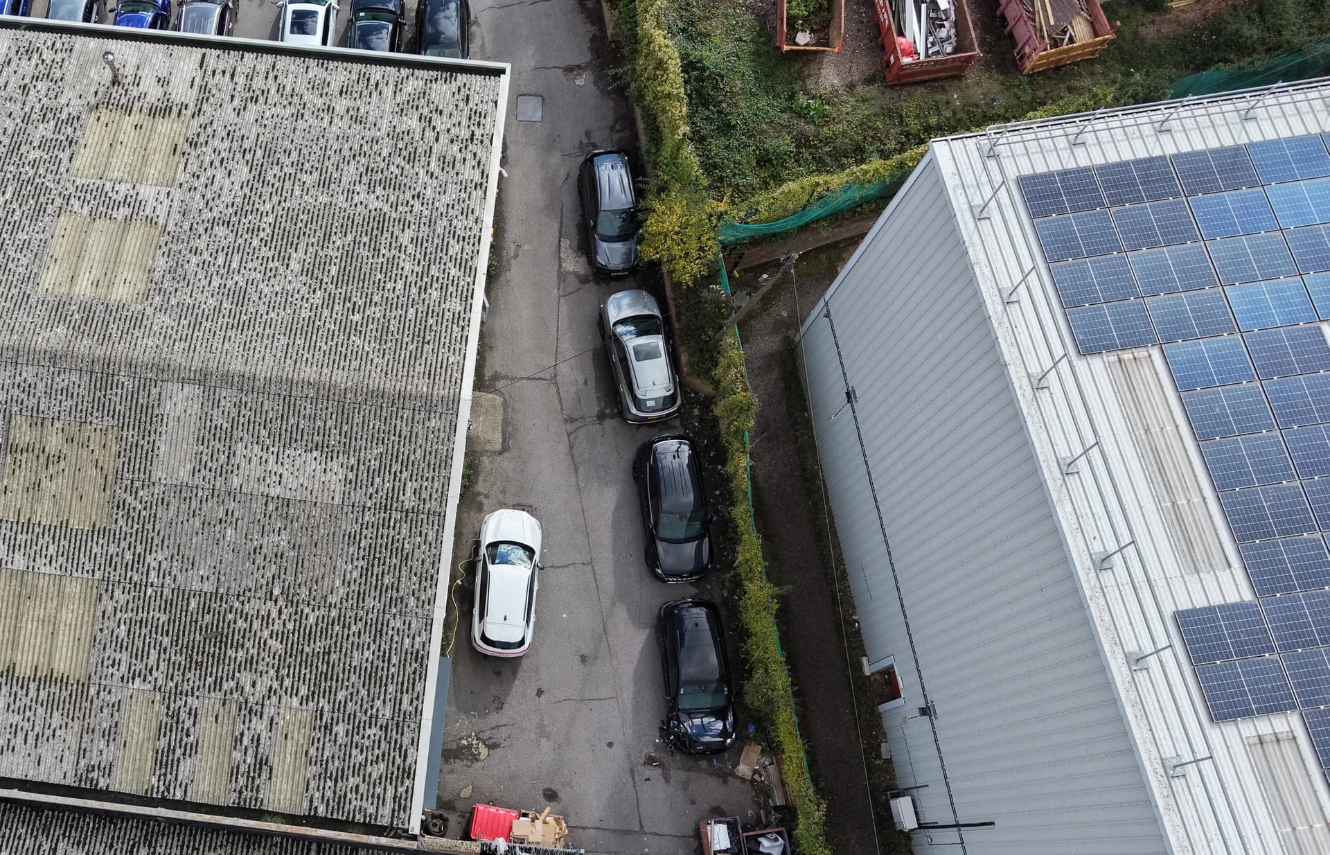 Wide top-down aerial view of two roof ranges with a service lane and parked vehicles beside them