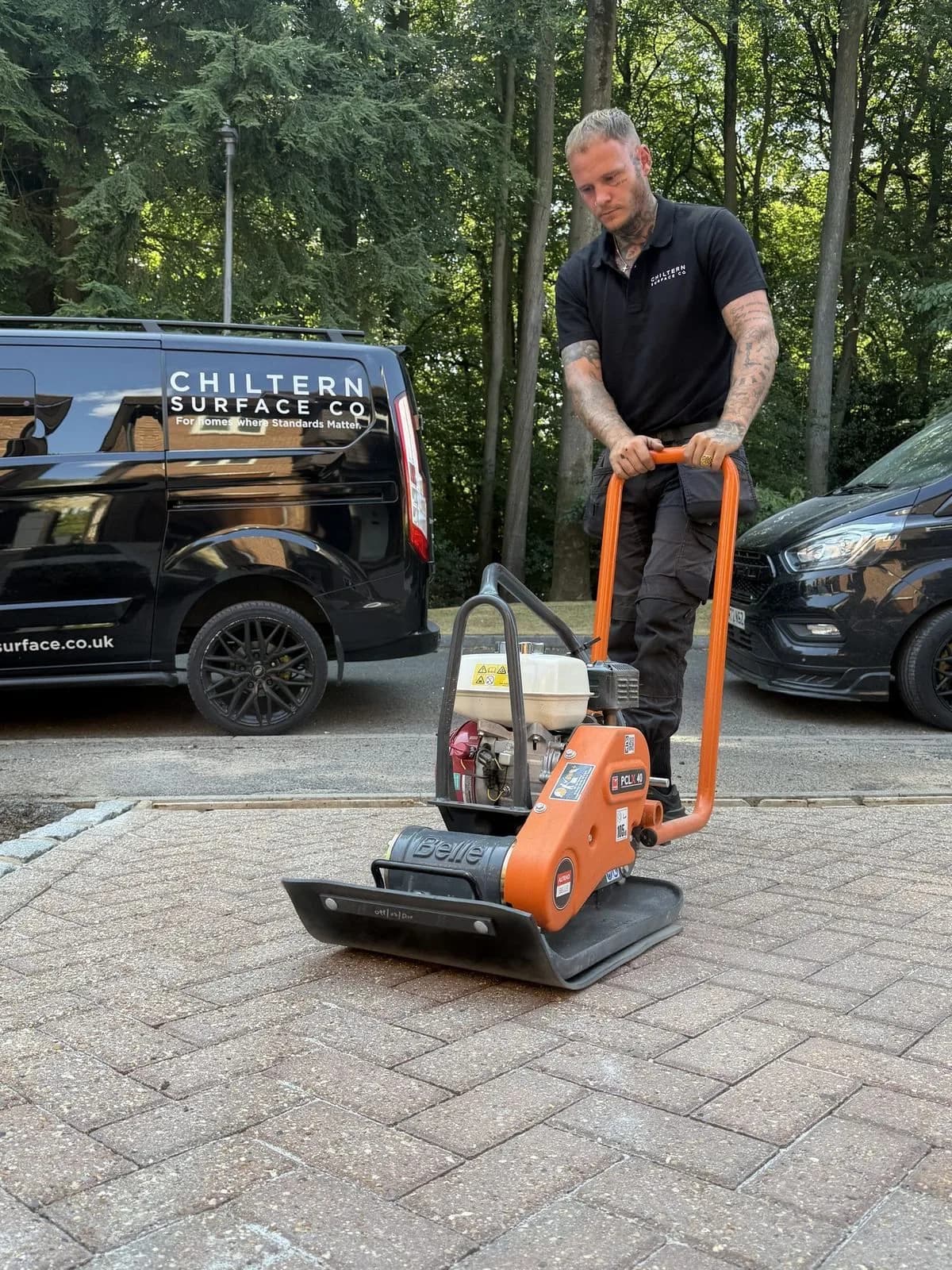 Chiltern Surface Co technician running the plate compactor across the re-sanded block paving, the company van behind