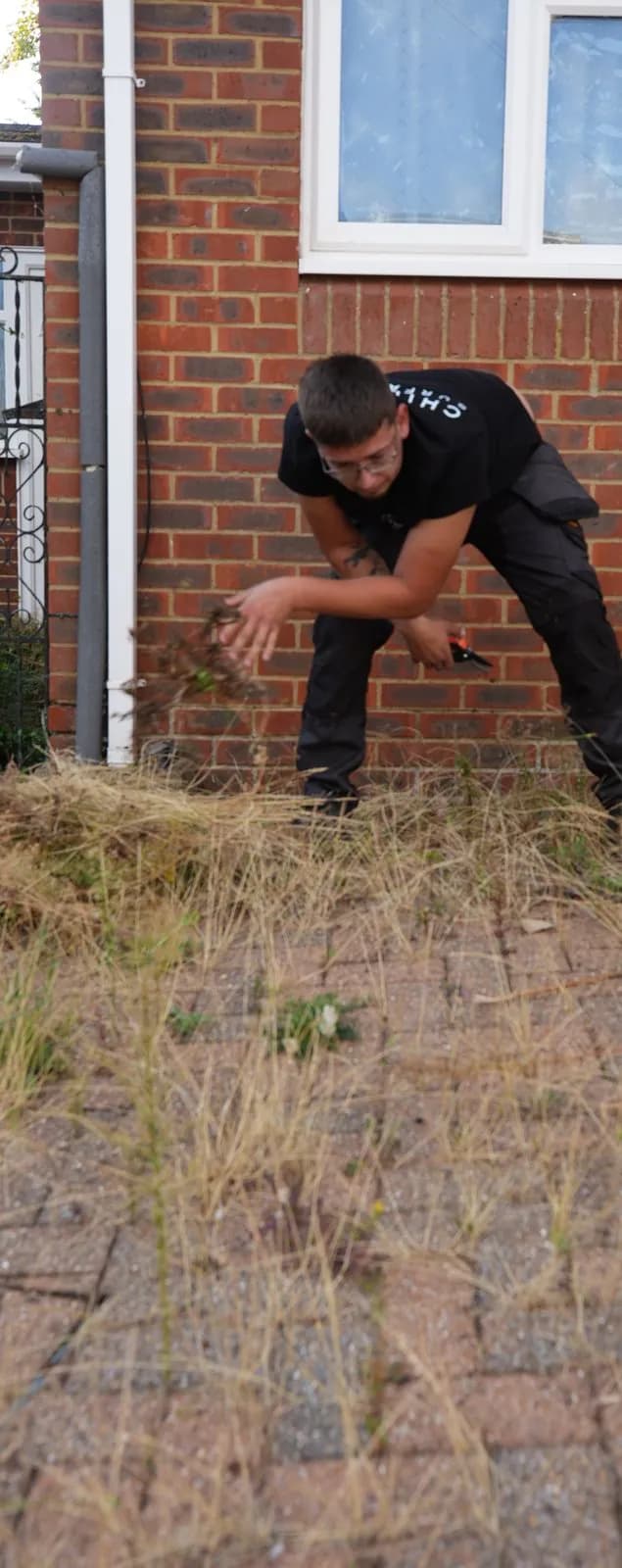 Chiltern Surface Co technician clearing grass and weeds from the driveway by hand
