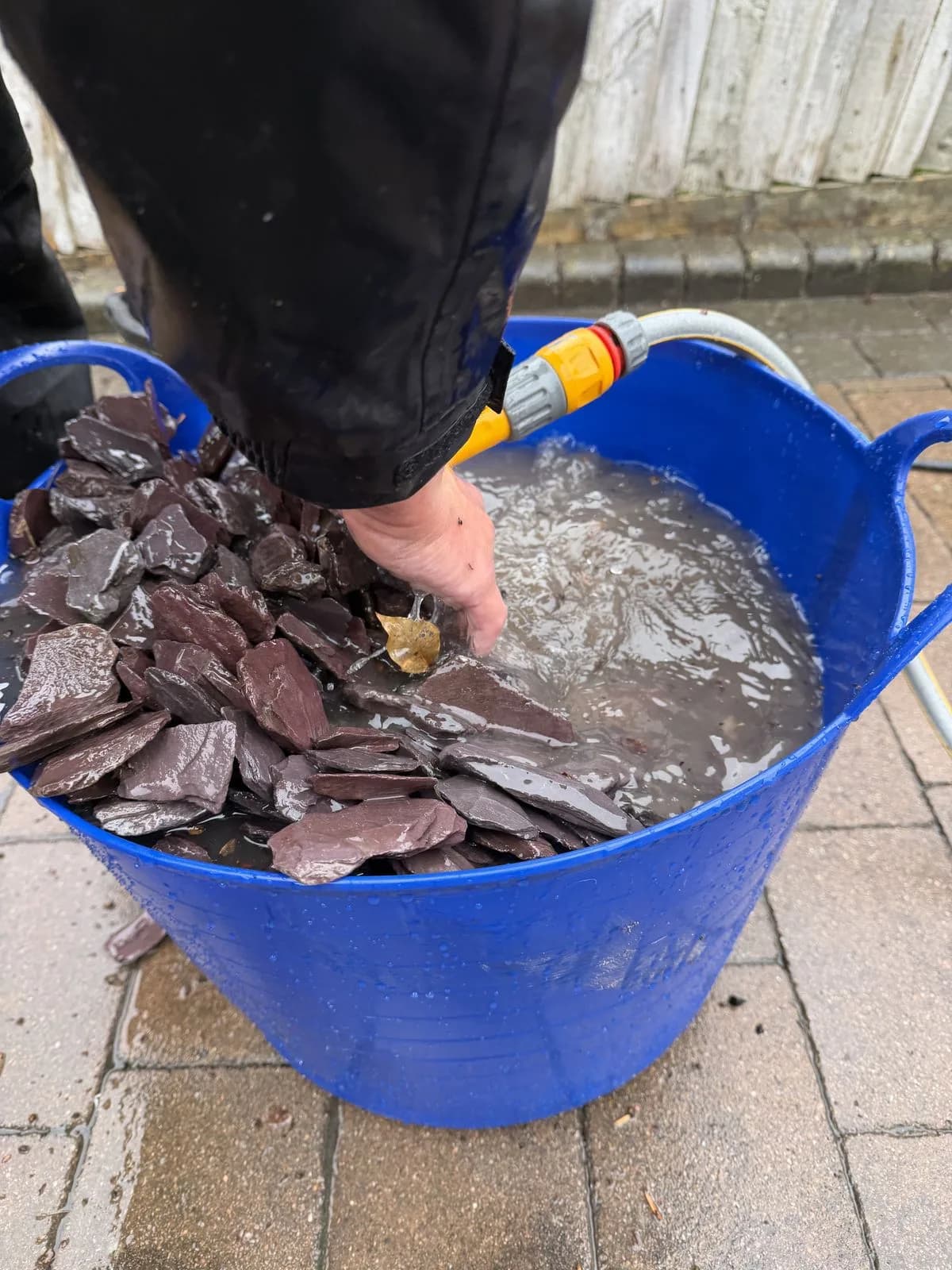 Slate edging from the High Wycombe driveway being washed piece by piece in a trug of clean water