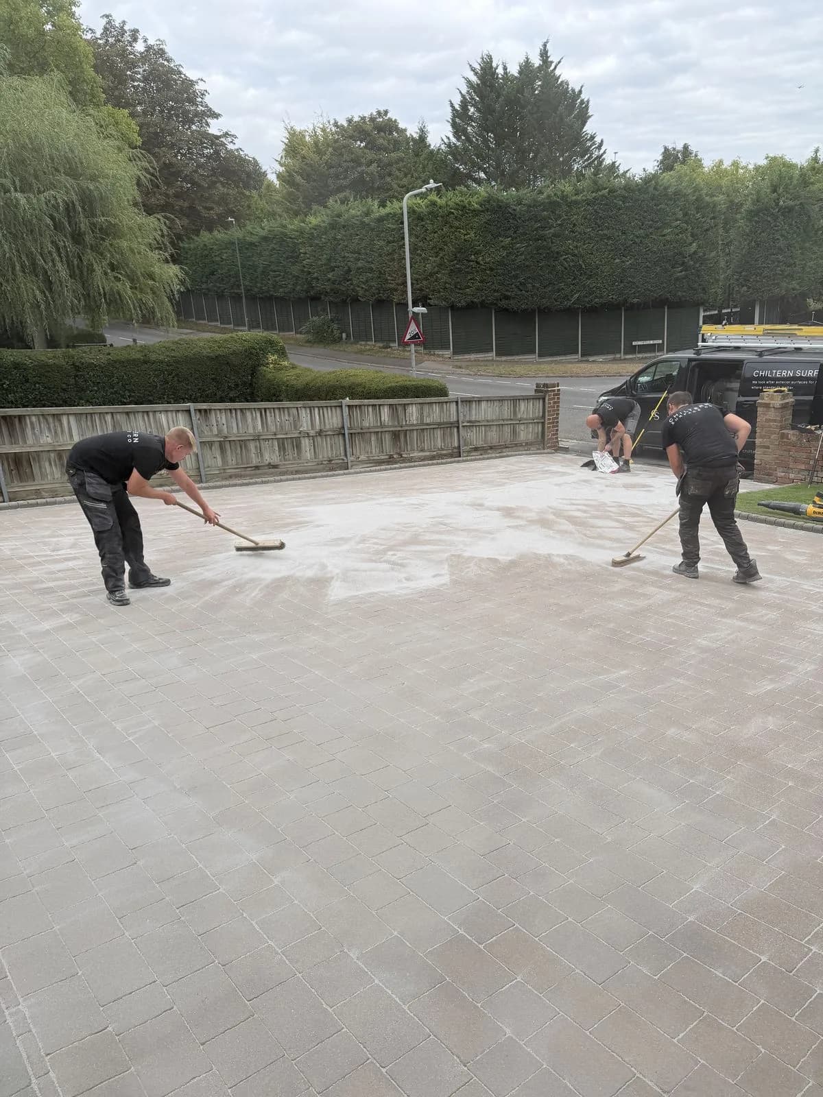 Chiltern Surface Co technicians brushing polymeric sand into the block paving joints across the driveway