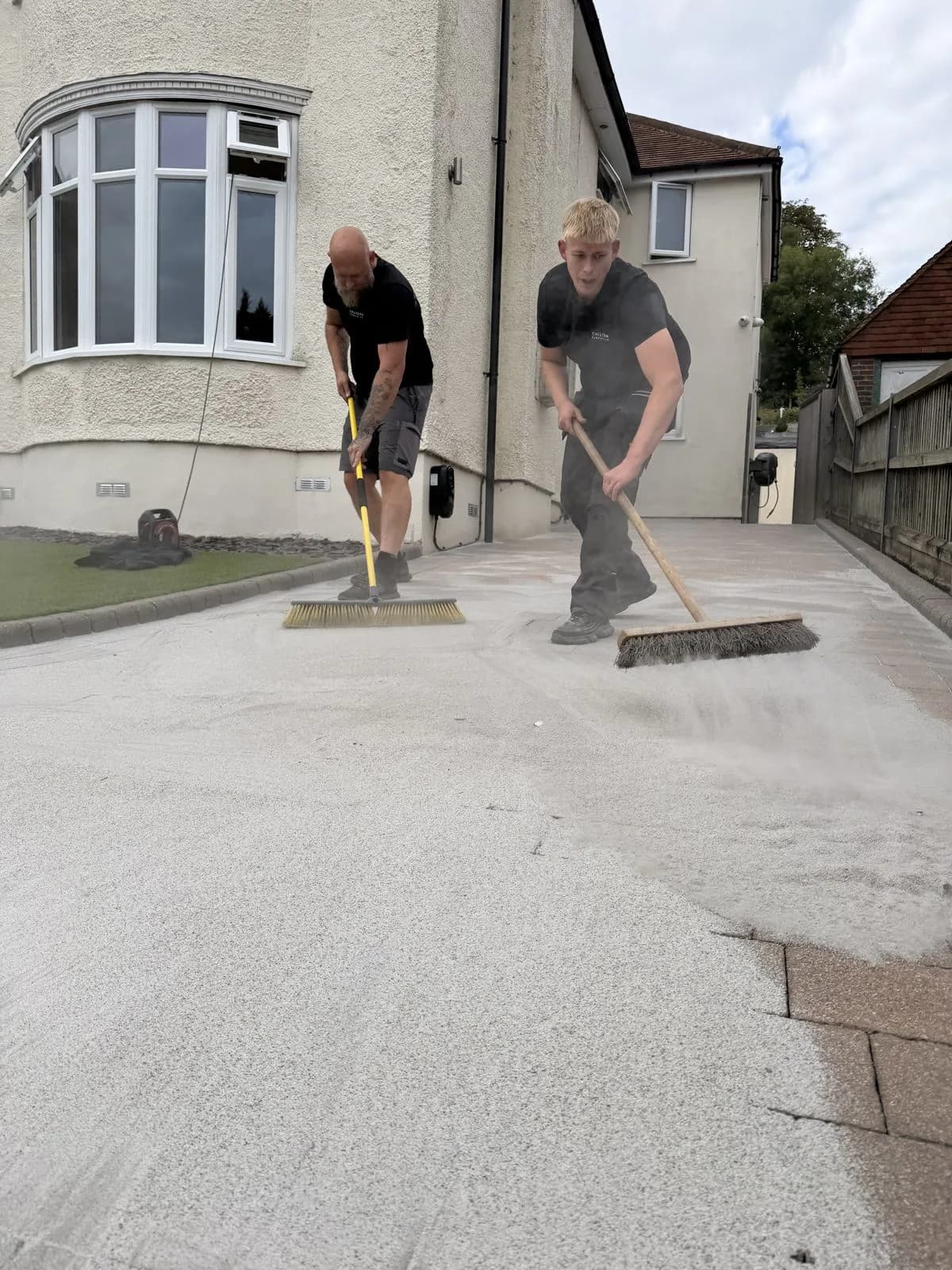 Chiltern Surface Co technicians brushing the second application of polymeric sand into the joints