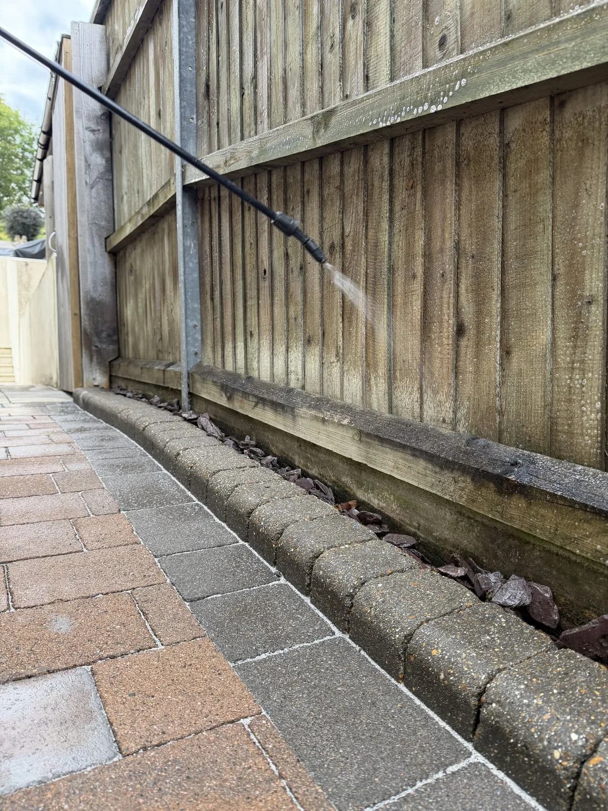 Biocide treatment being sprayed onto the adjacent fencing, with the cleaned slate edging reinstated below