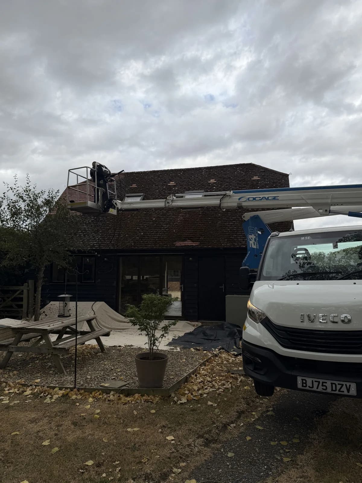 Truck-mounted cherry picker reaching over the steep clay tile roof in Aylesbury, with a Chiltern Surface Co technician working from the basket