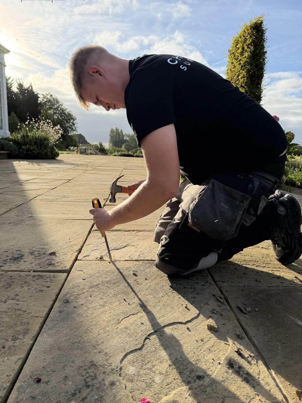 A Chiltern Surface Co technician chiselling the failed jointing out of the Indian sandstone patio