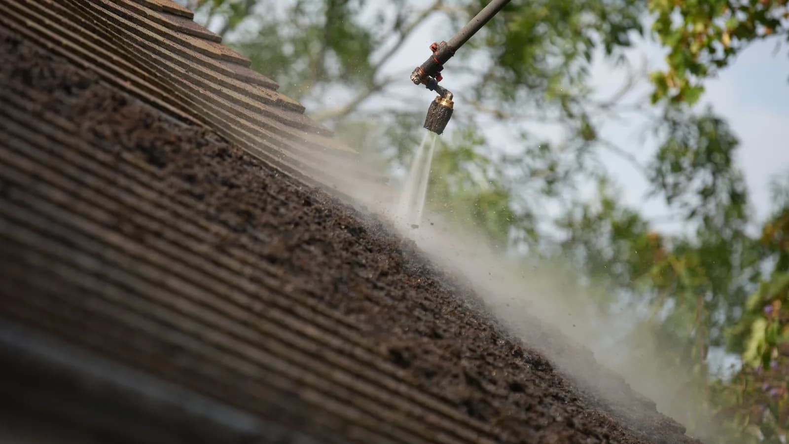 Close-up of the lance lifting thick moss from the concrete roof tiles, debris flying from the roof