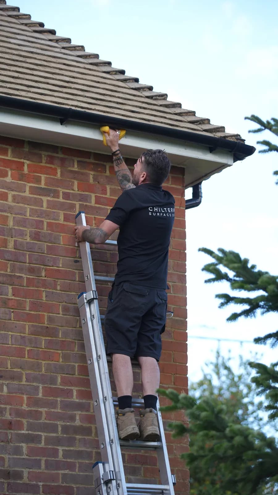 A Chiltern Surface Co technician cleaning the fascias and gutter exteriors from a ladder after the roof clean