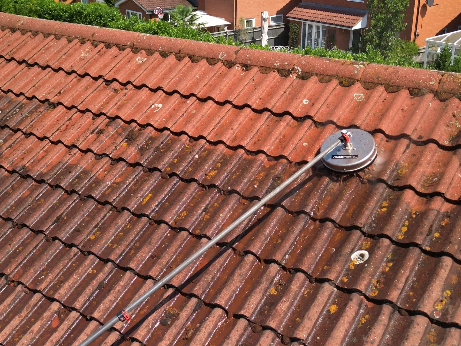 Rotary roof-cleaning head part-way across a concrete tile roof, clean tiles above and moss below