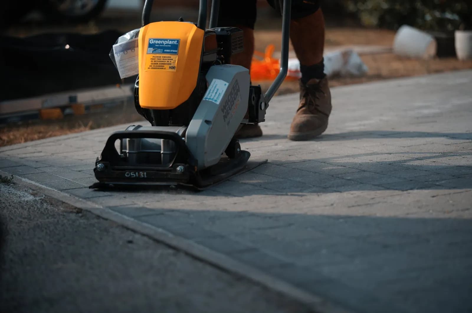 Plate compactor on the block paved driveway, settling the blocks and driving polymeric sand into the joints
