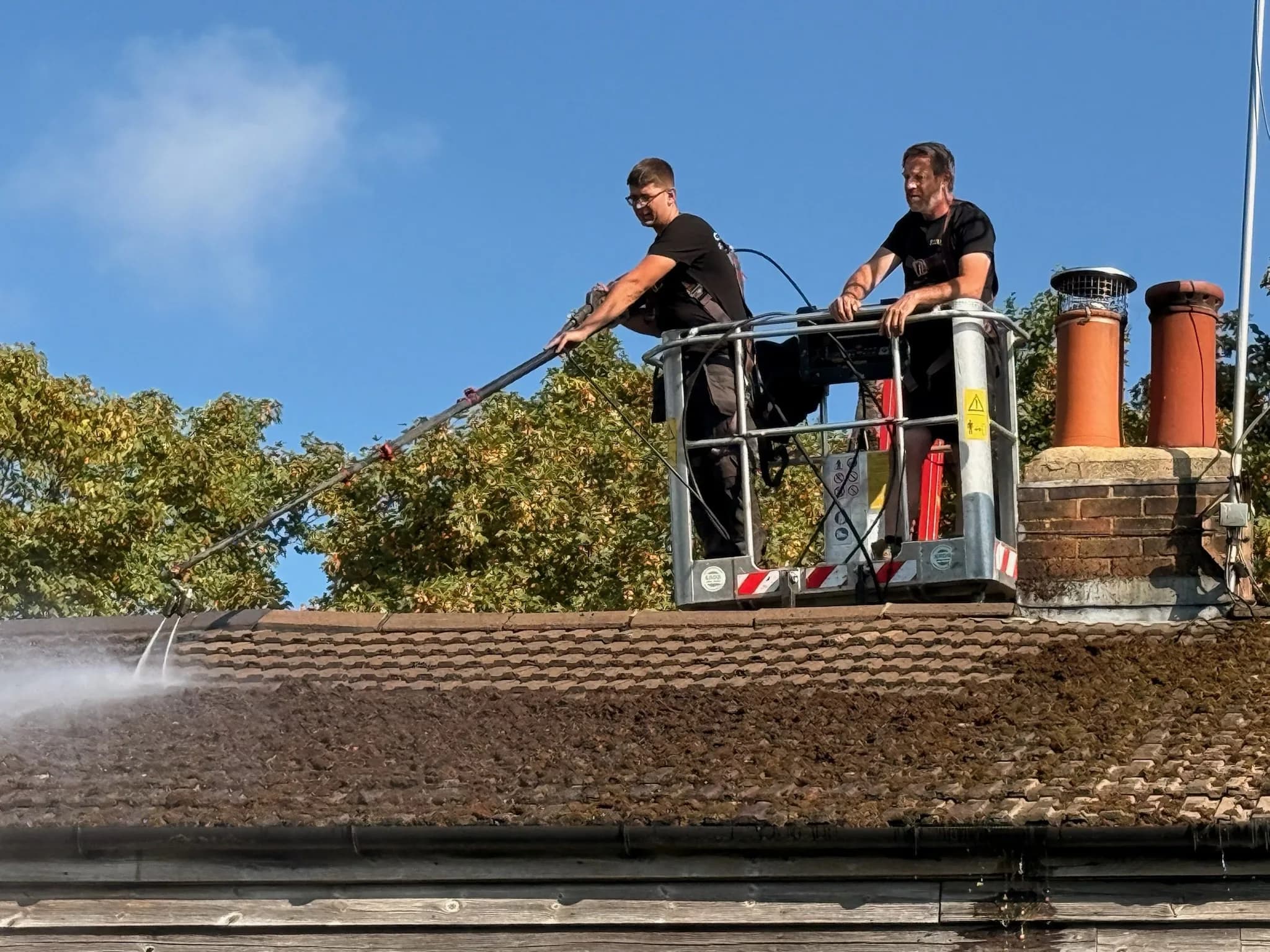Two Chiltern Surface Co technicians in a spider lift basket removing moss from the roof with a low-pressure lance