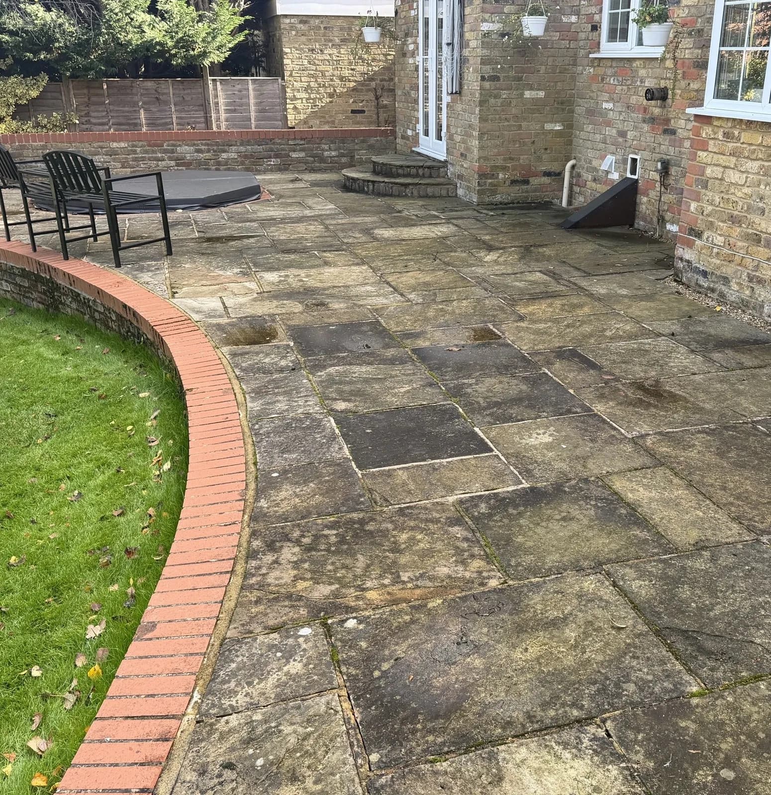 The sandstone patio along the curved brick edging the day before the works — black with growth, algae and lichen
