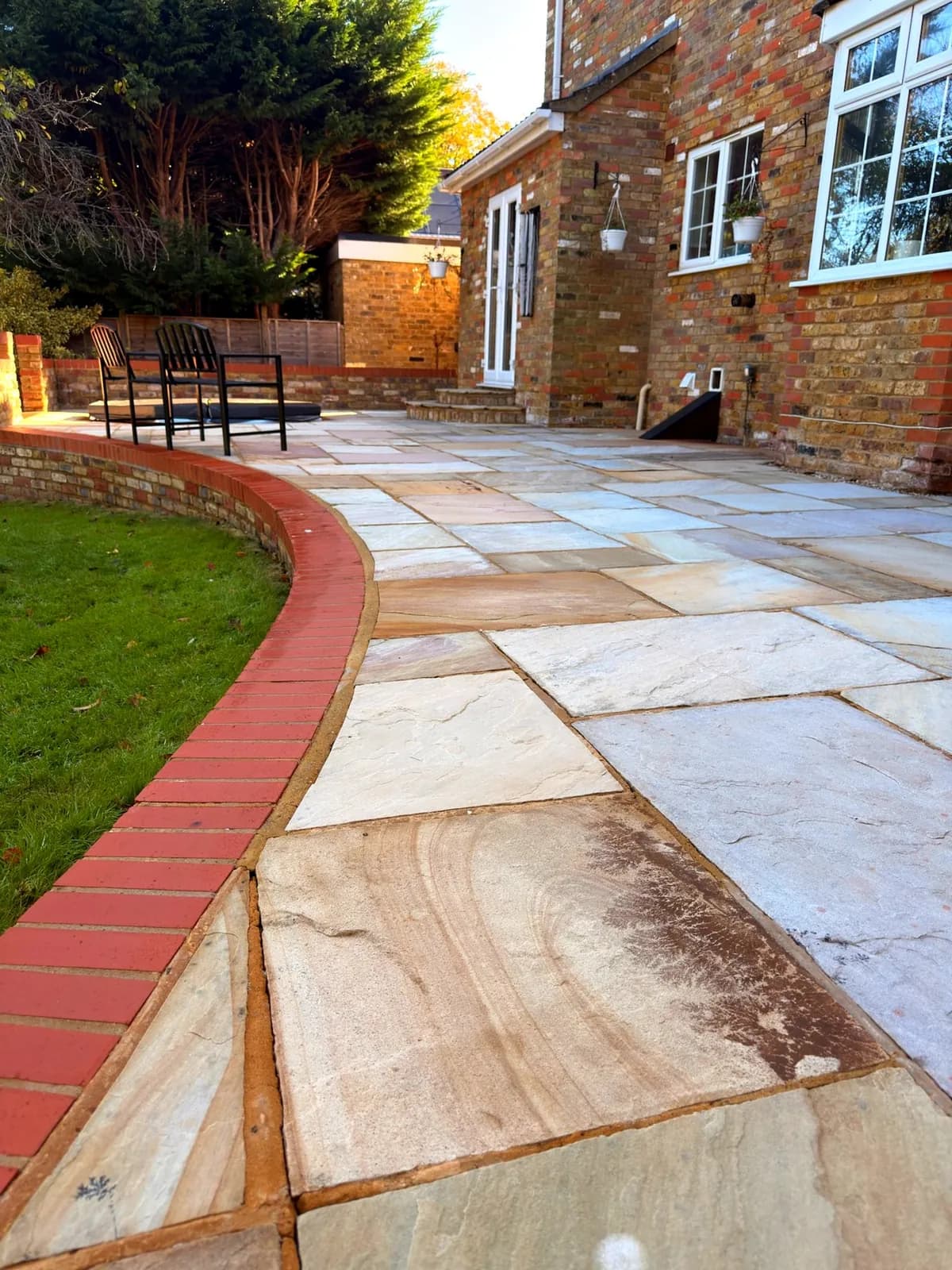 The finished Indian sandstone patio in Princes Risborough in autumn sun, curving along the red brick edging and lawn towards the house