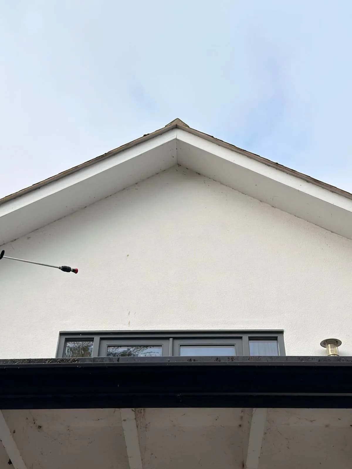 Chiltern Surface Co technician soft washing the rendered gable with a telescopic lance from the ground