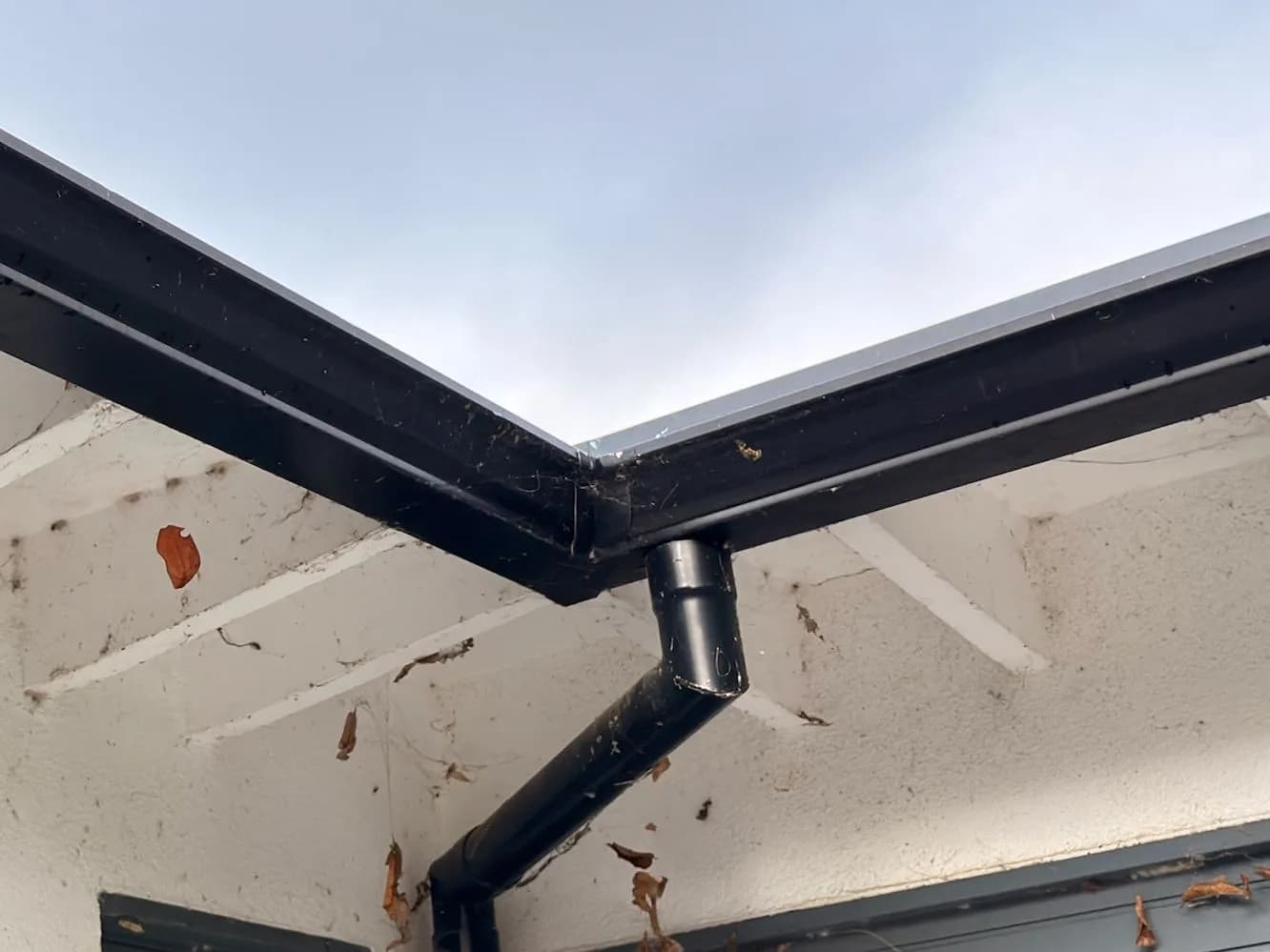 The gutter junction before cleaning, packed with leaves, webs and debris