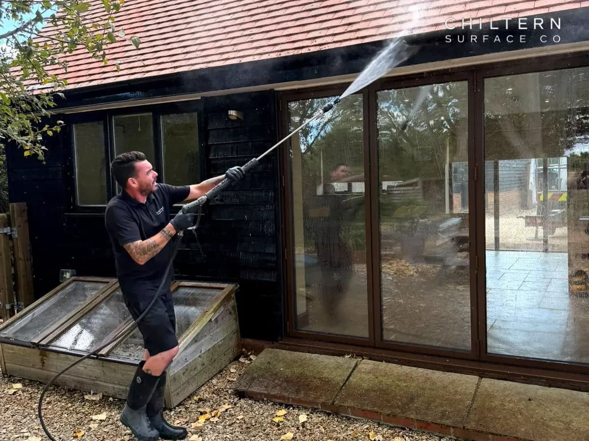 Operative with a long lance spraying the eaves of a black timber-clad building below a clay tiled roof