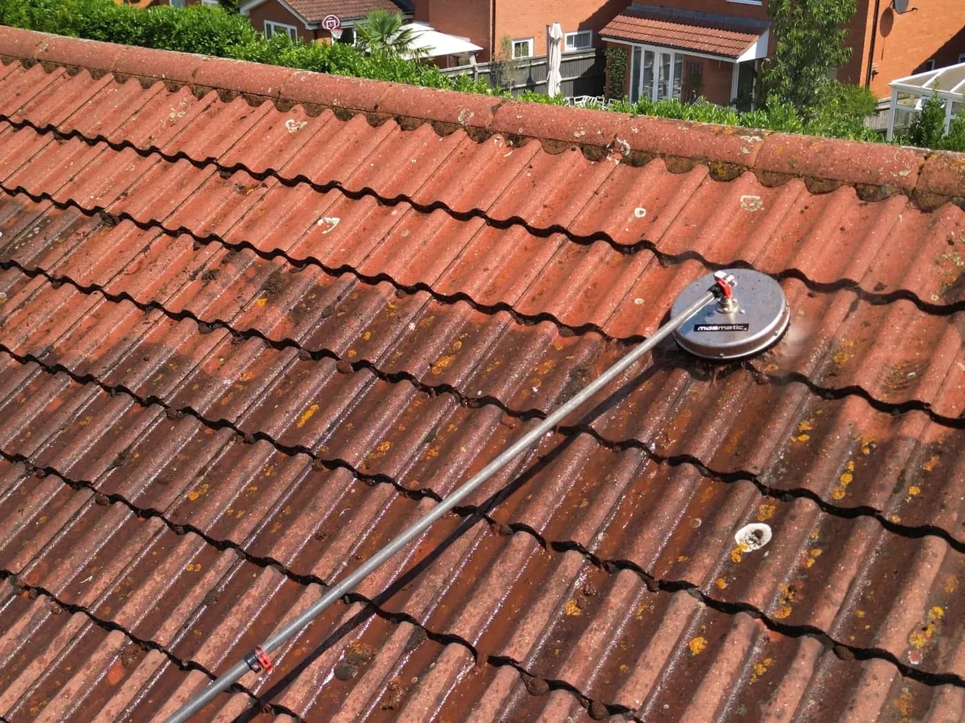 Rotary cleaning head part-way across a concrete tile roof, cleaned tiles beside the mossy section
