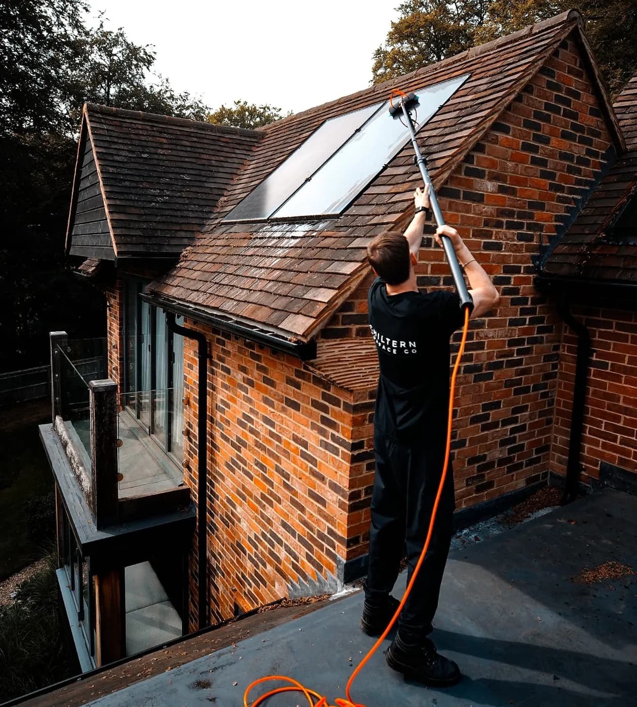 Water-fed pole and soft brush working across solar panels on a tiled roof