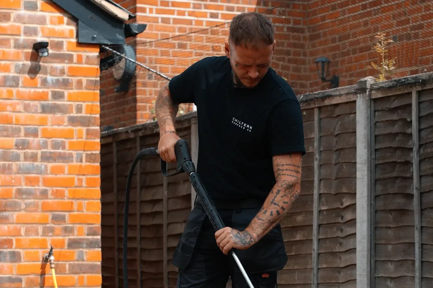 Operative pressure washing a natural stone patio beside a brick wall